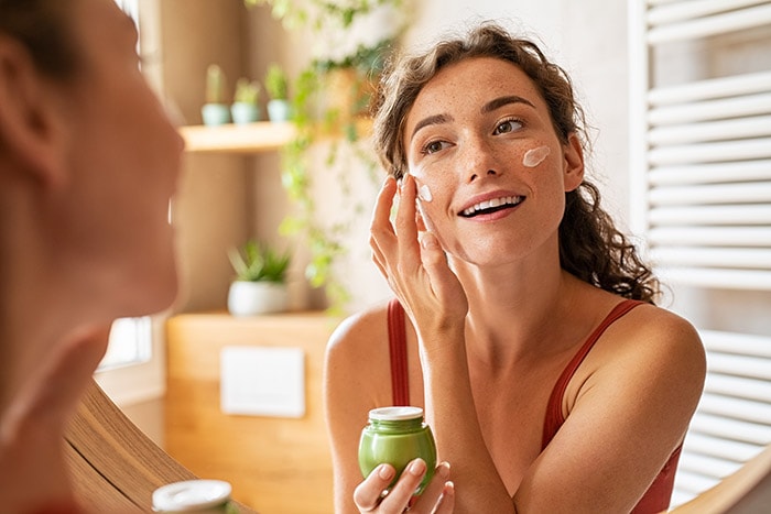 Woman applying moisturizer to her face, illustrating an essential step in skincare after receiving Profhilo treatment