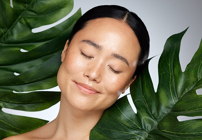 Woman's face with closed eyes, framed by tropical leaves, symbolising tranquility and rejuvenation