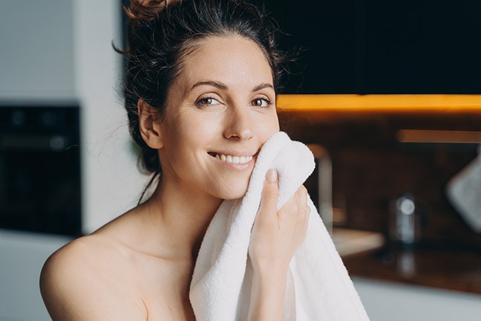 Woman gently cleansing her face, embodying a skincare routine crucial for post-Profhilo treatment care.