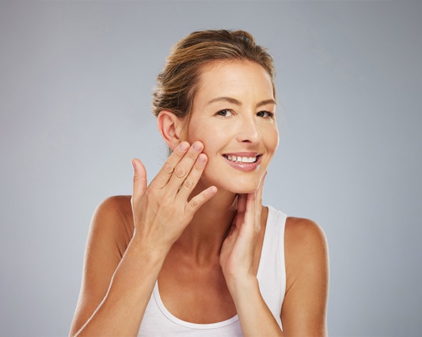 Middle-aged woman happily examining her rejuvenated skin in the mirror, touching her face, reflecting the youth-enhancing effects of Profhilo.